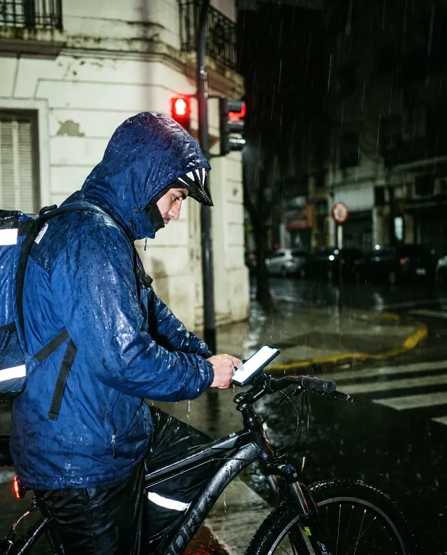 Un repartidor en bicicleta espera en un semáforo bajo la lluvia
